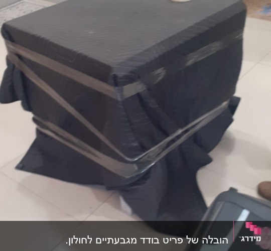 קופסה עטופה בבד שחור עם סרט דבק, על רצפה לבנה